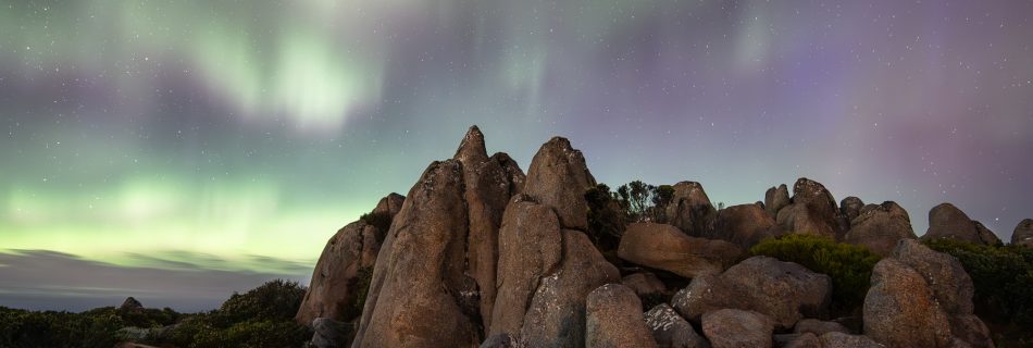 Purple-green aurora illuminating rocky peak in Tasmania