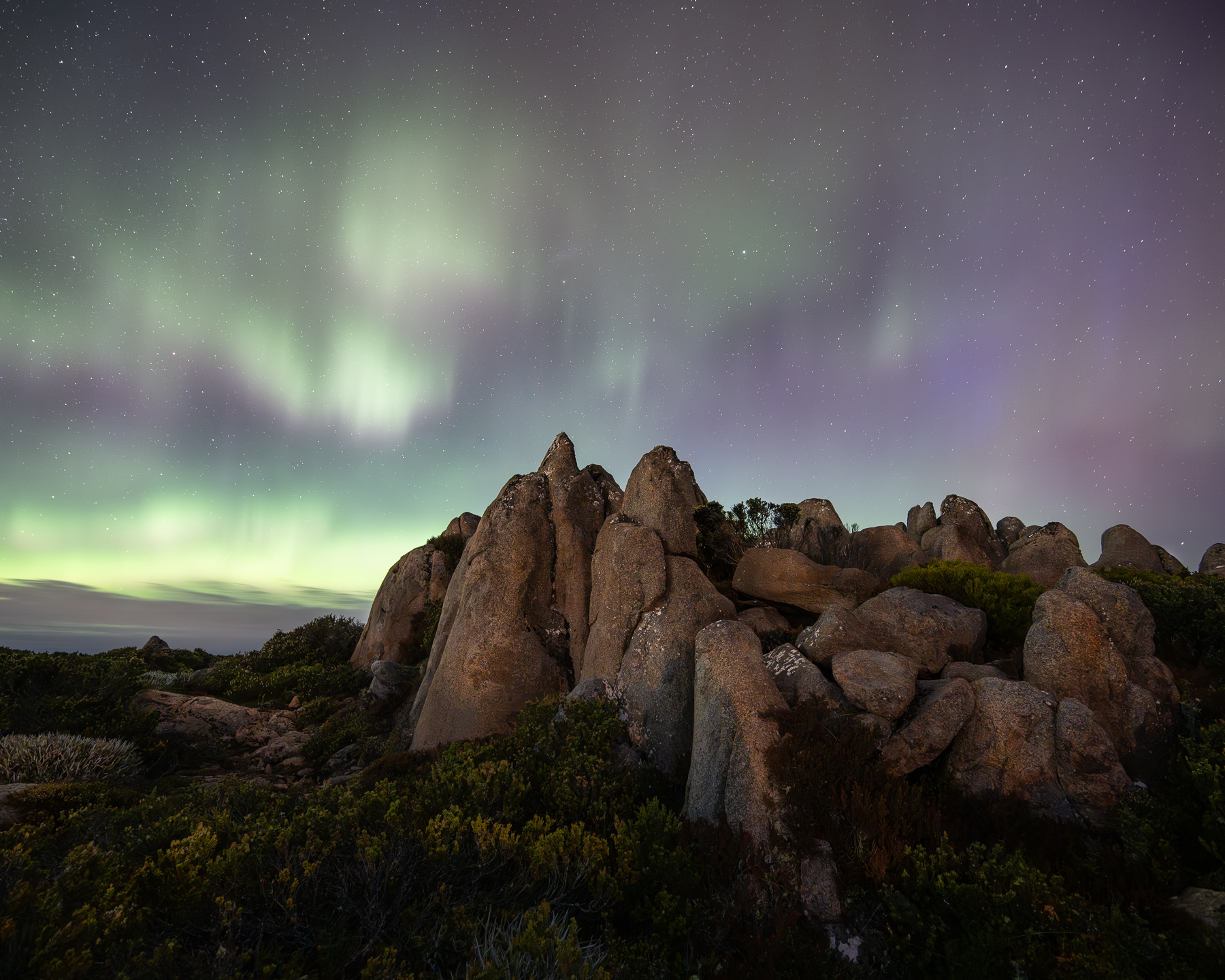 Purple-green aurora illuminating rocky peak in Tasmania