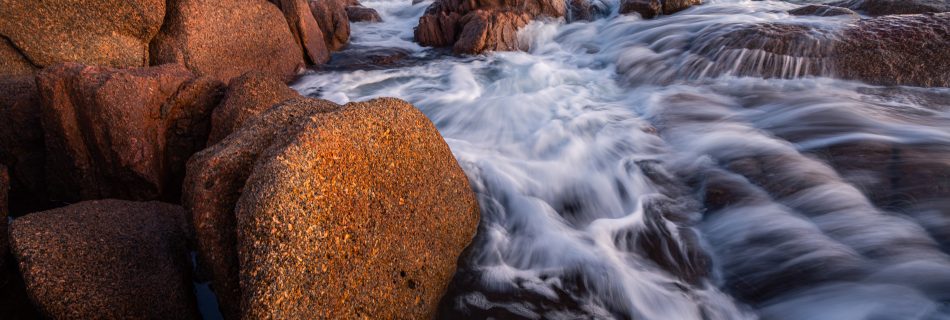 Golden sunset light over Coles Bay with pink granite peaks reflected in calm Tasmanian coastal waters